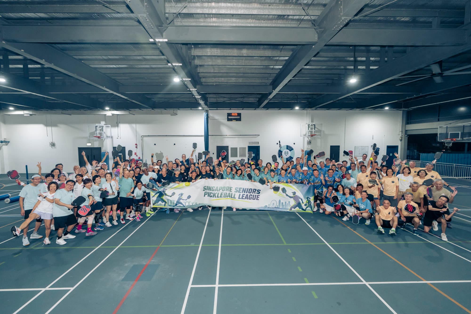 Players and supporters from the participating clubs gather at Dover Court for the opening night of the Singapore Seniors Pickleball League, holding their paddles high beneath the league banner.
